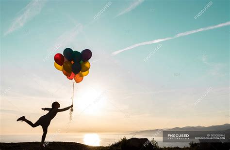 Mädchen In Silhouette Spielt Bei Sonnenuntergang Mit Luftballons