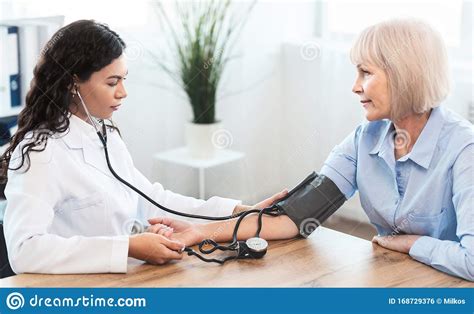 Female Nurse Checking Blood Pressure Of Mature Woman Stock Photo