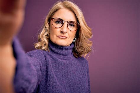 middle age beautiful blonde woman wearing sweater and glasses make selfie by the camera with a