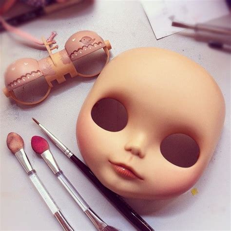 A Dolls Face Is Shown Next To Makeup Brushes And Other Items On A Table
