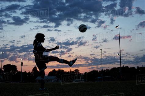 Side View Of Girl Kicking Soccer Ball At Field Against Sky During