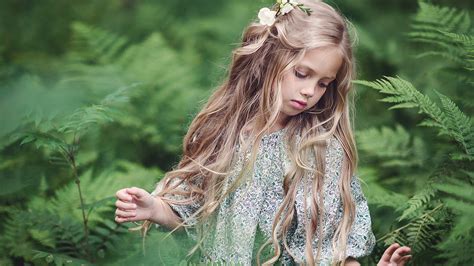 Blonde Cute Little Girl Is Touching Green Leaves Wearing White Green