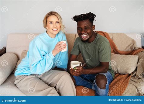 Hombre Negro Y Una Joven Rubia En El Sofá Llevan Tazas En Las Manos