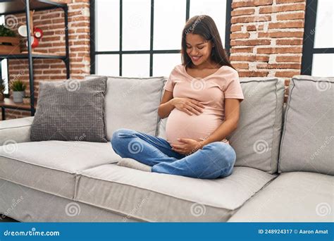 Young Latin Woman Pregnant Touching Belly Sitting On Sofa At Home Stock