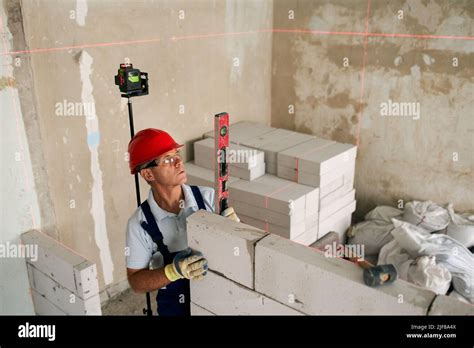 Bricklayer Or Mason Lays Bricks To Construct Wall Of Autoclaved Aerated