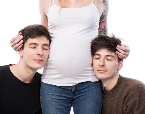 한 명의 아내와 두 명의 남편이 있는 현대적인 일부다처제 가족 흰색 배경에 두 젊은 남자와 함께 포즈를 취하는 젊은 임산부 프리미엄 사진