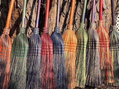 Several Colorful Brooms Lined Up In Front Of A Stone Wall With Grass