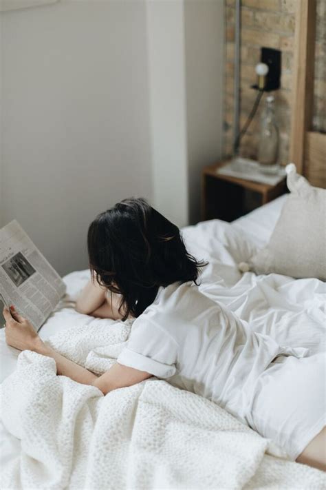 A Woman Laying In Bed While Reading A Book With Her Head On The Pillow And Arms Behind Her Back