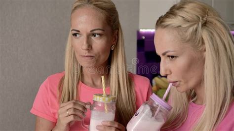 The Blonde Twin Sisters Drink A Milkshake From A Glass With Tubes