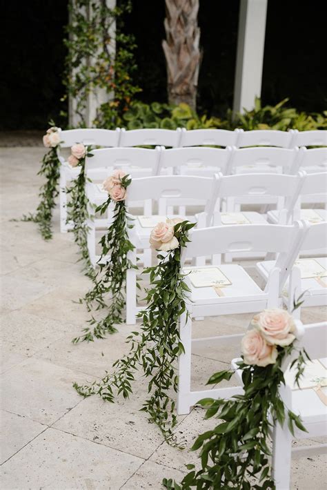 Rows Of White Chairs Decorated With Flowers And Greenery