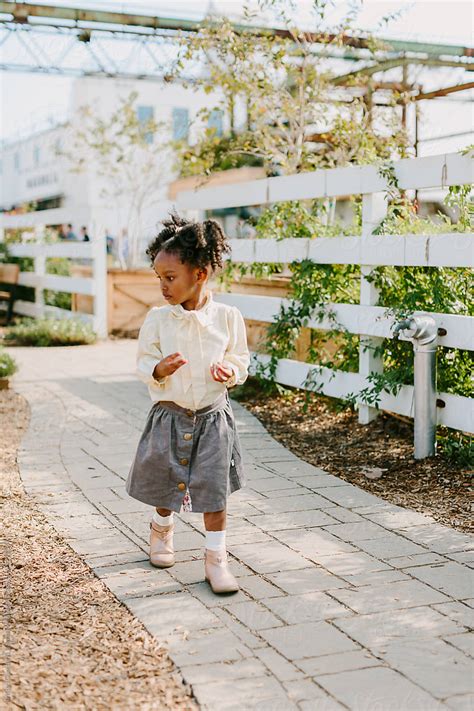 A Little Adorable Girl In Stylish Clothes Walking On A Sidewalk By