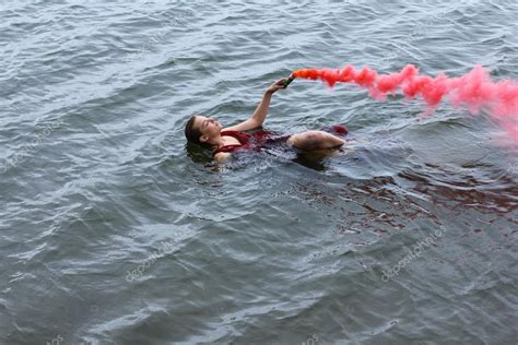 Young Beautiful Drowned Woman With Smoke Grenade In Red Dress Floating