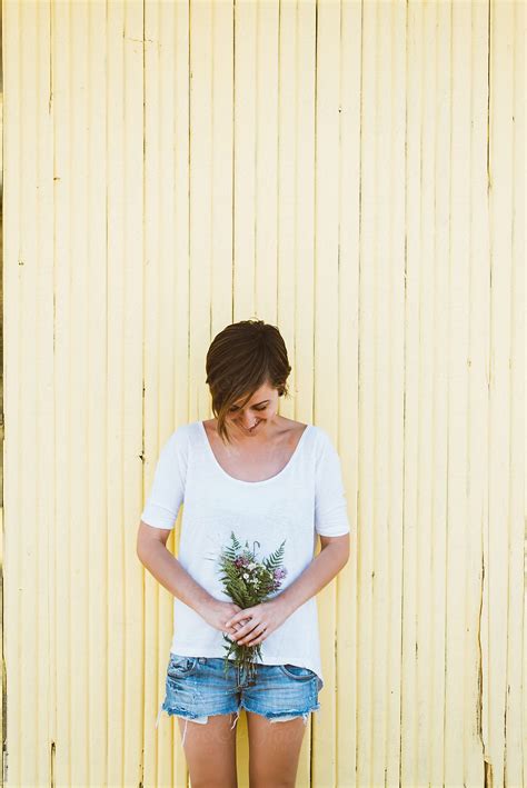 woman standing against the yellow wall with bouquet by stocksy contributor brkati krokodil