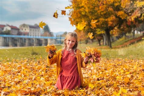 Happy Little Girl Playing With Fallen Yellow Leaves In Autumn Park