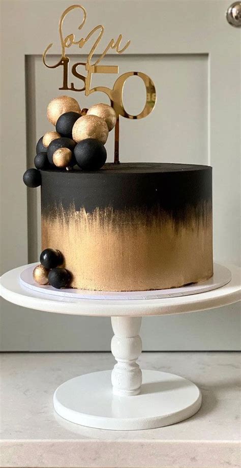 A Black And Gold Birthday Cake On A White Pedestal With The Number