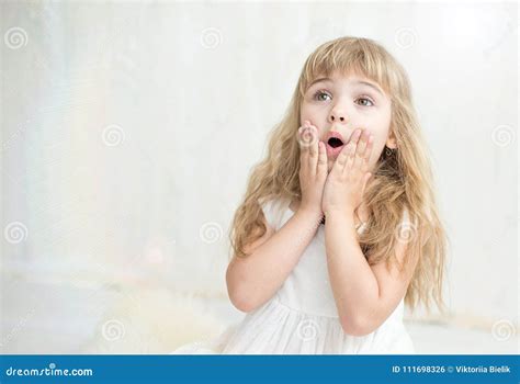 Портрет милой маленькой девочки в белом платье она удивлена и положила ее руки на щеки Стоковое