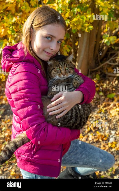 Portrait Of Smiling Girl Holding Tabby Cat Outdoors In Autumn Stock