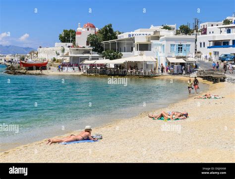People Sunbathing On Mykonos Town Beach And Whitewashed Seaside Stock