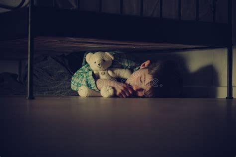 Muchacho Asustado Que Duerme Debajo De Su Cama Con Teddy Bear Foto De