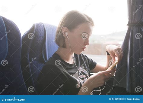 Young Girl Sits In The Bus At The Window Uses A Smartphone And Listens To Music In The