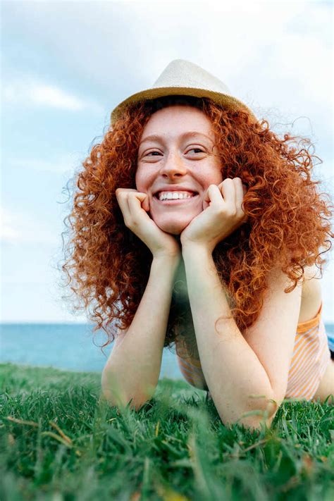 Happy Curly Redhead Haired Female With Freckles Lying On Lawn Looking