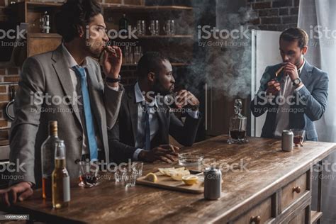 Young Multiethnic Businessmen Smoking Cigars And Drinking Alcohol While