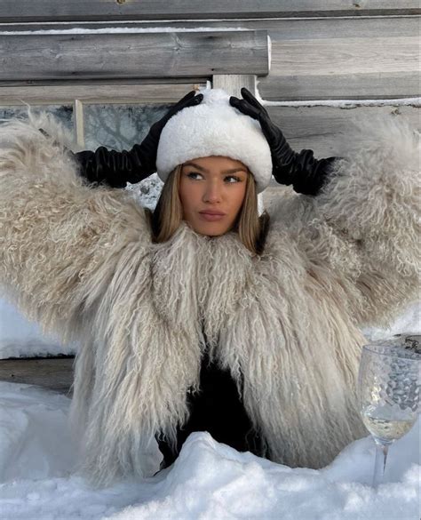 a woman sitting in the snow wearing a furry coat and holding a glass of wine