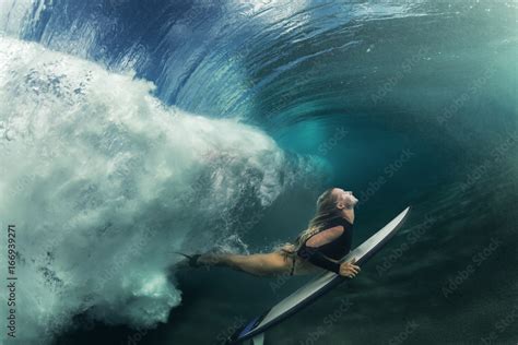 a blonde surfer girl underwater doing duck dive holding surfing board left behind air bubbles in