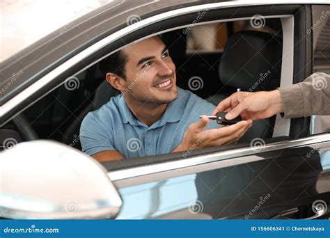 Young Giving Car Key To Customer In Modern Auto Dealership Closeup