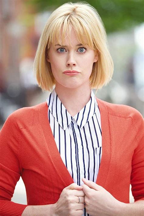 A Woman With Blonde Hair Wearing A Red Cardigan And Striped Shirt Posing For The Camera