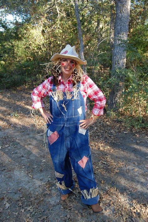 a woman wearing overalls and a hat standing in the woods