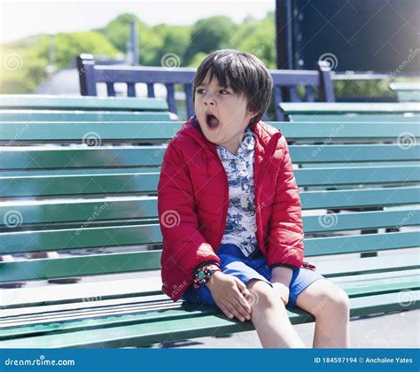 Portrait Child Boy Yawning While Sitting On Metal Bench In The Park