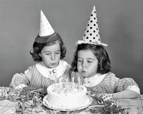 1960s Twin Girls Wearing Party Hats Blowing Out Candles On Birthday