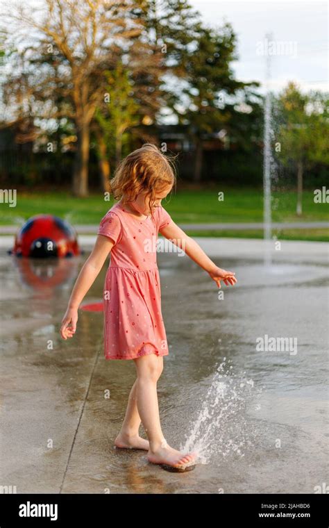 Little Girl Playing With Water At The Splash Pad In Summer Child At