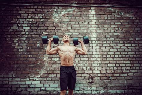 Muscular Guy Doing Exercises With Dumbbell Against A Brick Wall Stock