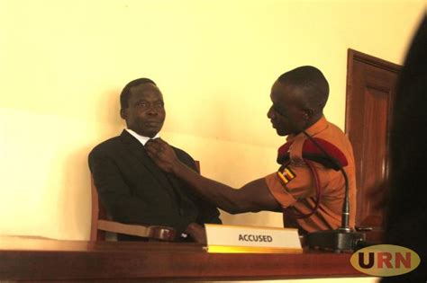 a prison warden helps thomas kwoyelo to adjust his neck tie while appearing before at gulu high