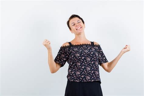 free photo mature woman in floral blouse and black skirt showing winner gesture and looking