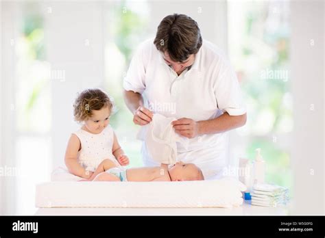 Father Changing Diaper To Baby Boy Little Girl Helping Dad To Change