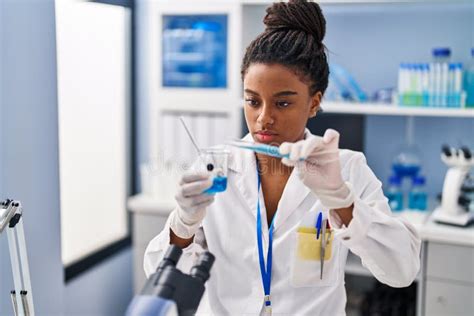 African American Woman Scientist Pouring Liquid On Glass At Laboratory