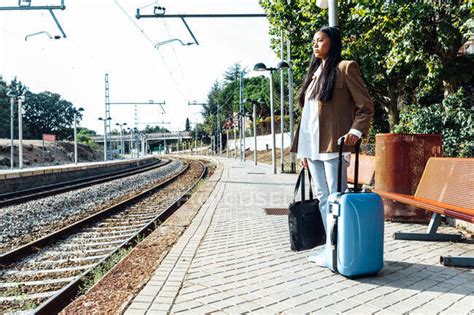 Side View Of Asian Female Traveler With Suitcase Standing On Platform Of Railroad Station While