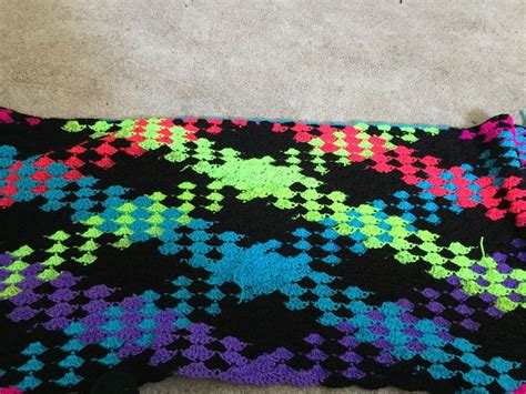 A Colorful Knitted Blanket Laying On Top Of A Floor Next To A Pair Of