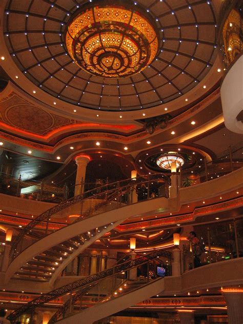 The Inside Of A Cruise Ship With Stairs And Chandelier