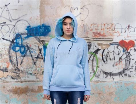 Blue Haired Teenage Girl In Light Blue Oversize Hoodie Pointing Against Graffiti Wall Stock