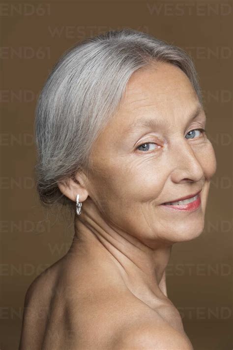 Portrait Of Naked Senior Woman With Grey Hair In Front Of Brown Background Stock Photo