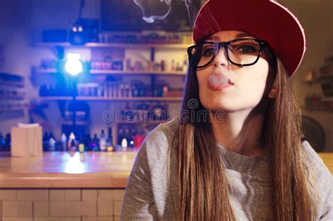 Young Pretty Woman In Red Cap Smoke An Electronic Cigarette At The Vape