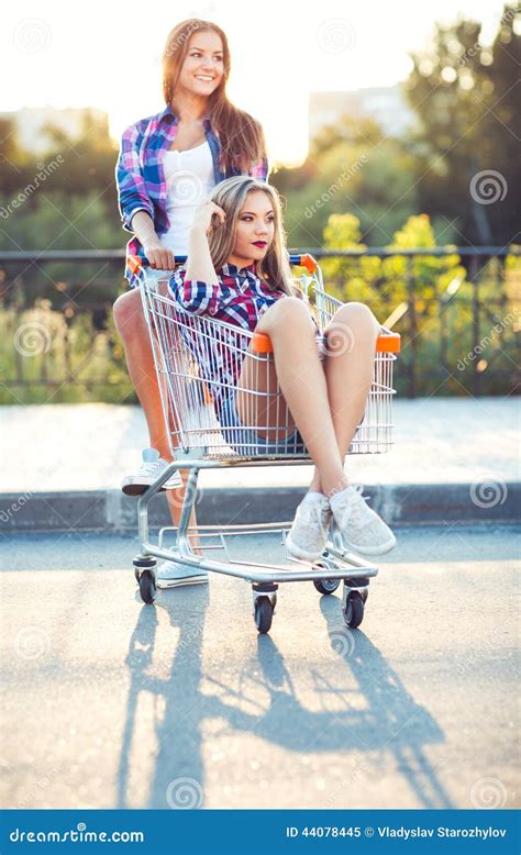 Two Happy Beautiful Teen Girls Driving Shopping Cart Outdoors Stock