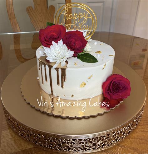 A White Cake With Red Roses On Top And Gold Decoration Is Sitting On A