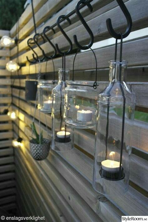 some glass jars with candles hanging on the side of a wall next to a wooden fence