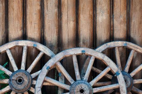 Three Old Wooden Wheels From Carts On A Log Wall Background Stock Image
