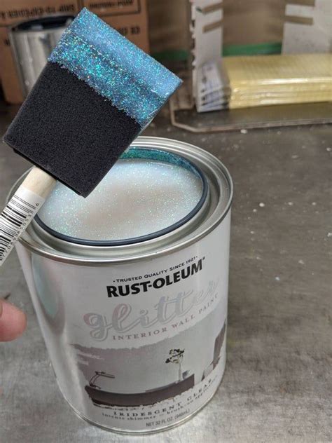 A Person Holding A Paint Brush Over A Can